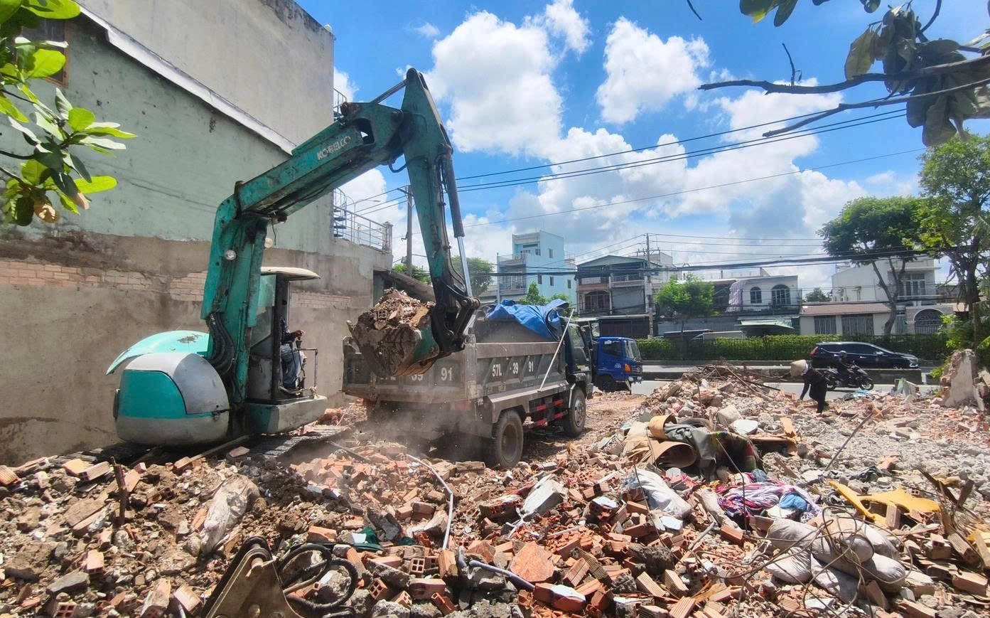 Máy xúc đang xúc xà bần lên xe tải tại một mặt bằng vừa tháo dỡ bên Quốc lộ 22