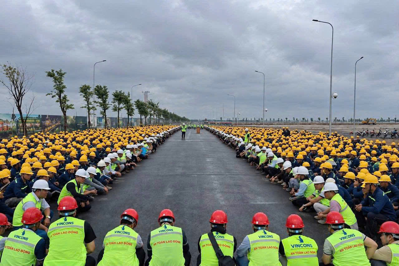 Hàng trăm công nhân và kỹ sư đội mũ bảo hộ ngồi xếp hàng hai bên con đường mới trải nhựa trên công trường Vinhomes Saigon Park