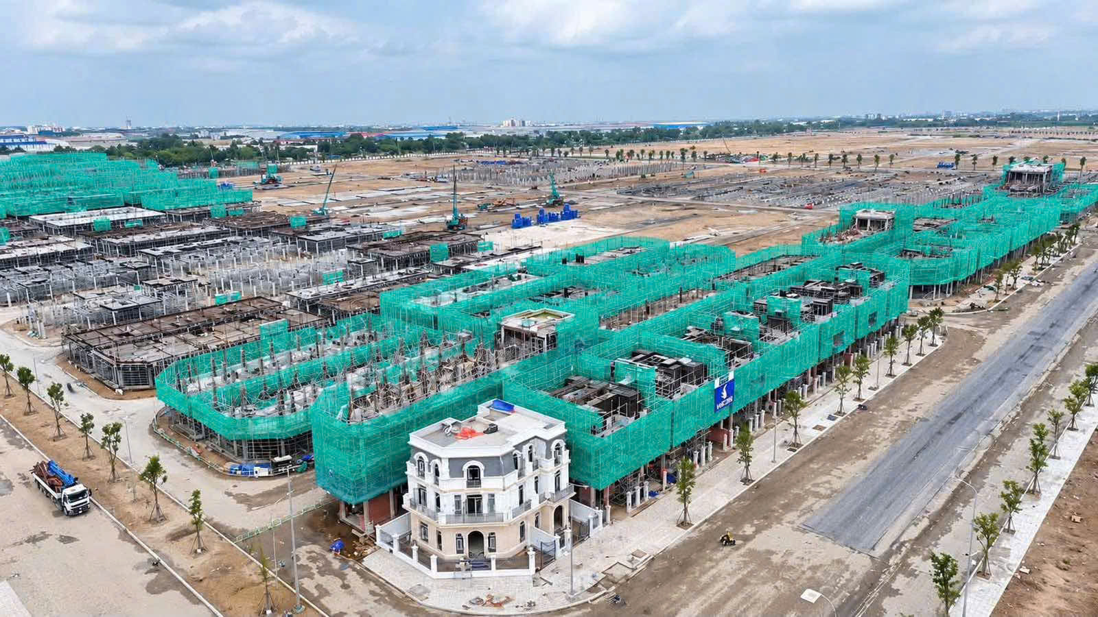 Ảnh chụp từ trên cao công trường Vinhomes Saigon Park Hóc Môn, nhiều dãy nhà liền kề đang xây phủ lưới xanh, đường nội khu và kênh nước bên cạnh